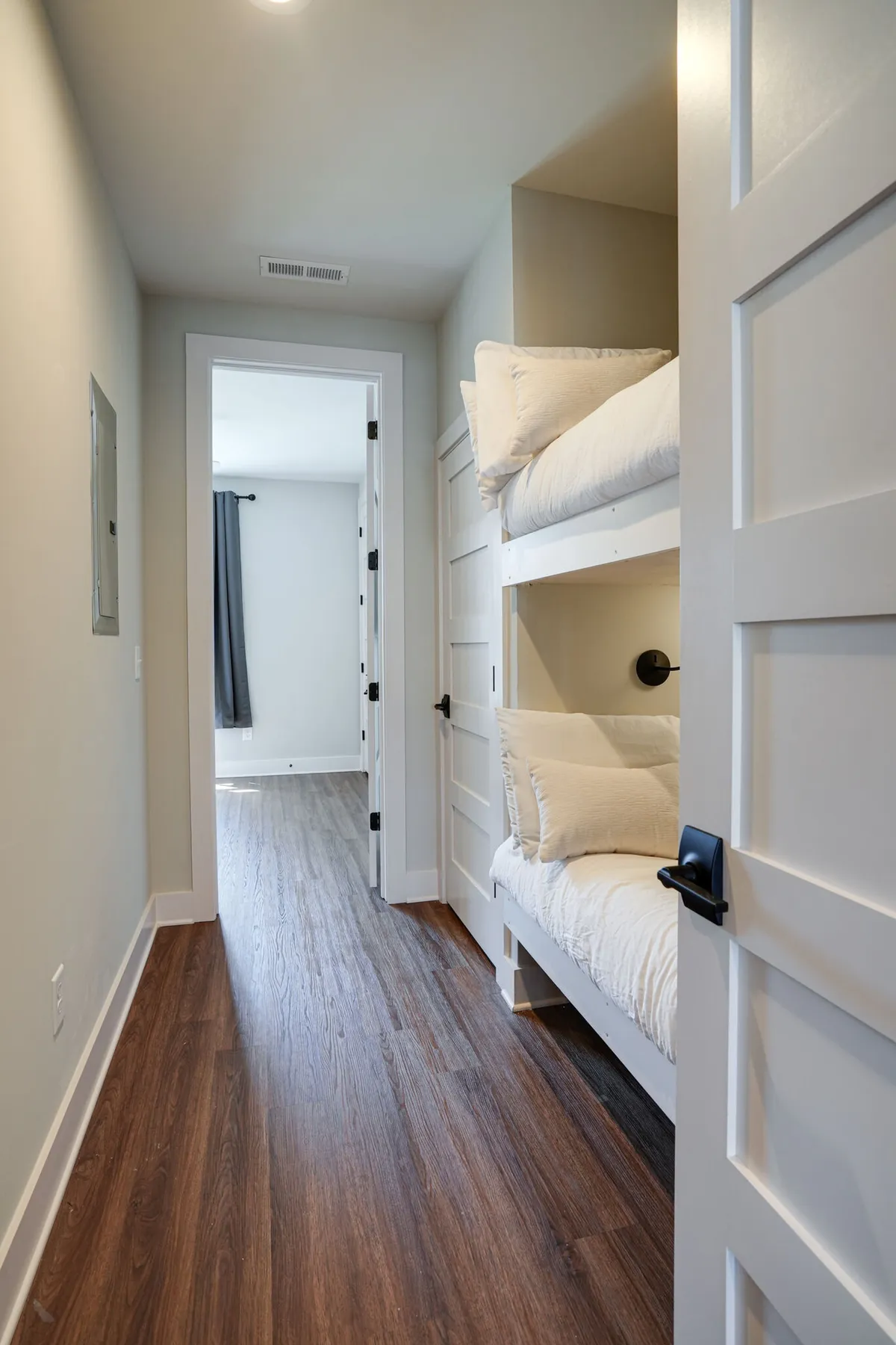 A close-up interior view of a bunk bed area, showing the sturdy structure of the bunks and a glimpse through a doorway into the rest of the home. The scene evokes a sense of privacy and coziness, suggesting a dedicated space for younger guests or friends.