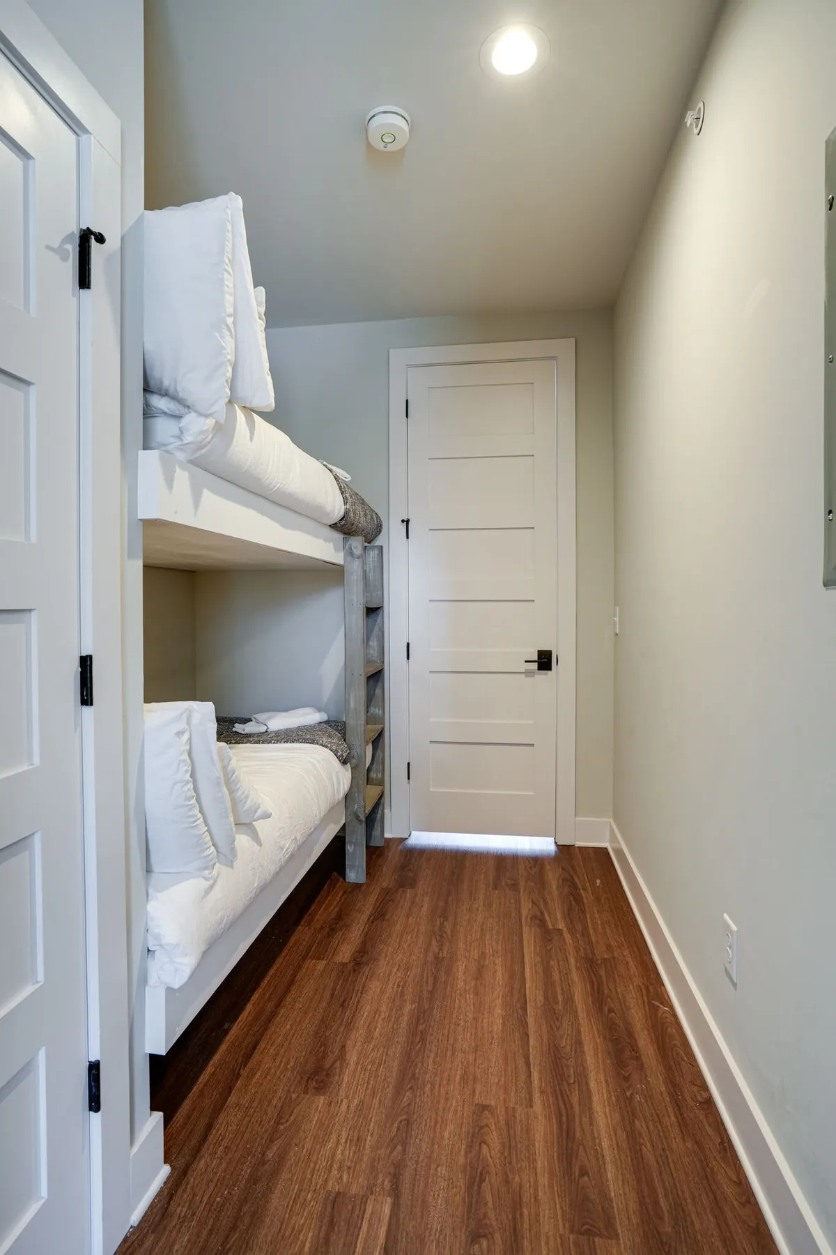 A cozy nook with twin bunk beds, dressed in crisp white linens and set against warm wooden flooring. The bunk beds are inviting and suggest a playful, family-friendly space—perfect for kids or friends sharing a room. The simple decor creates a sense of warmth and comfort.