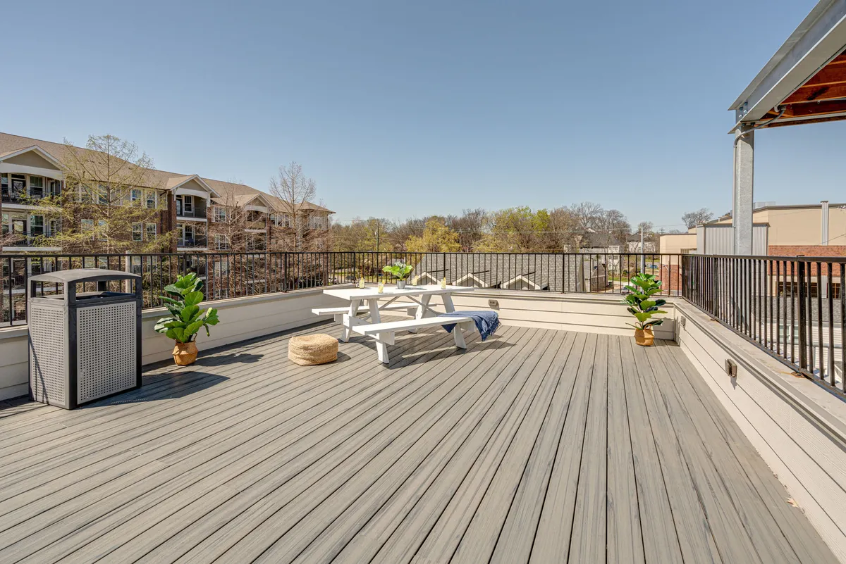 A cheerful rooftop scene with a picnic table surrounded by planters, and a soft golden sunset in the background. The setting is relaxed and inviting, ideal for a quiet coffee or conversation while soaking in the evening glow.