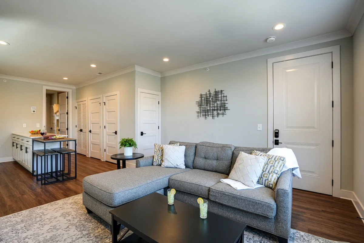 The hero image captures a stylish and comfortable interior living space featuring a plush grey sectional sofa, a sleek black coffee table, and eye-catching decorative wall art. The setting exudes a sense of relaxation and warmth, perfectly suited for socializing, unwinding after a day in the city, or enjoying cozy movie nights. Soft lighting and tasteful décor create an inviting and modern ambiance.