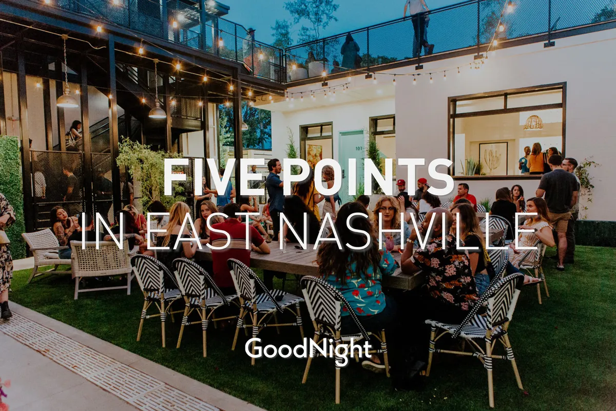A large outdoor dining table is set on a rooftop deck adorned with festive string lights. Groups of people are gathered around, socializing and enjoying dinner under the stars, creating a vibrant community atmosphere.